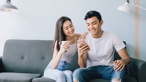 A young couple looks at a mobile phone while sitting on their sofa