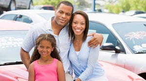 A family stands in front of a vehicle in a car lot