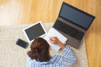 Brunette young student using her tablet and notebook for doing homework lying in the living room-1