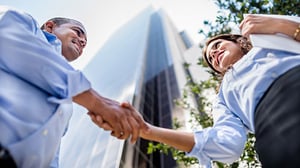 Two employees shake hands outside a large building