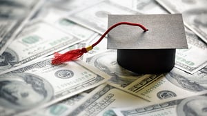 A graduation cap sits on top of one-hundred dollar bills