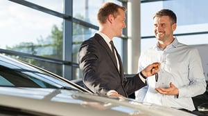 A car salesman hands keys to the new car's owner