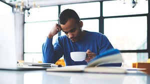 A young man sits reading a book while drinking coffee