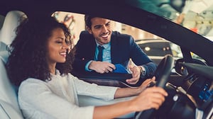 A woman is sitting behind the wheel of a new car while a salesperson shows her the vehicle