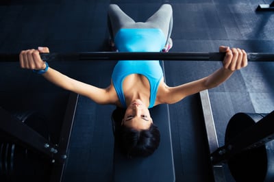 Young fit woman working out with barbell on bench in the gym. Bar Bench Pres